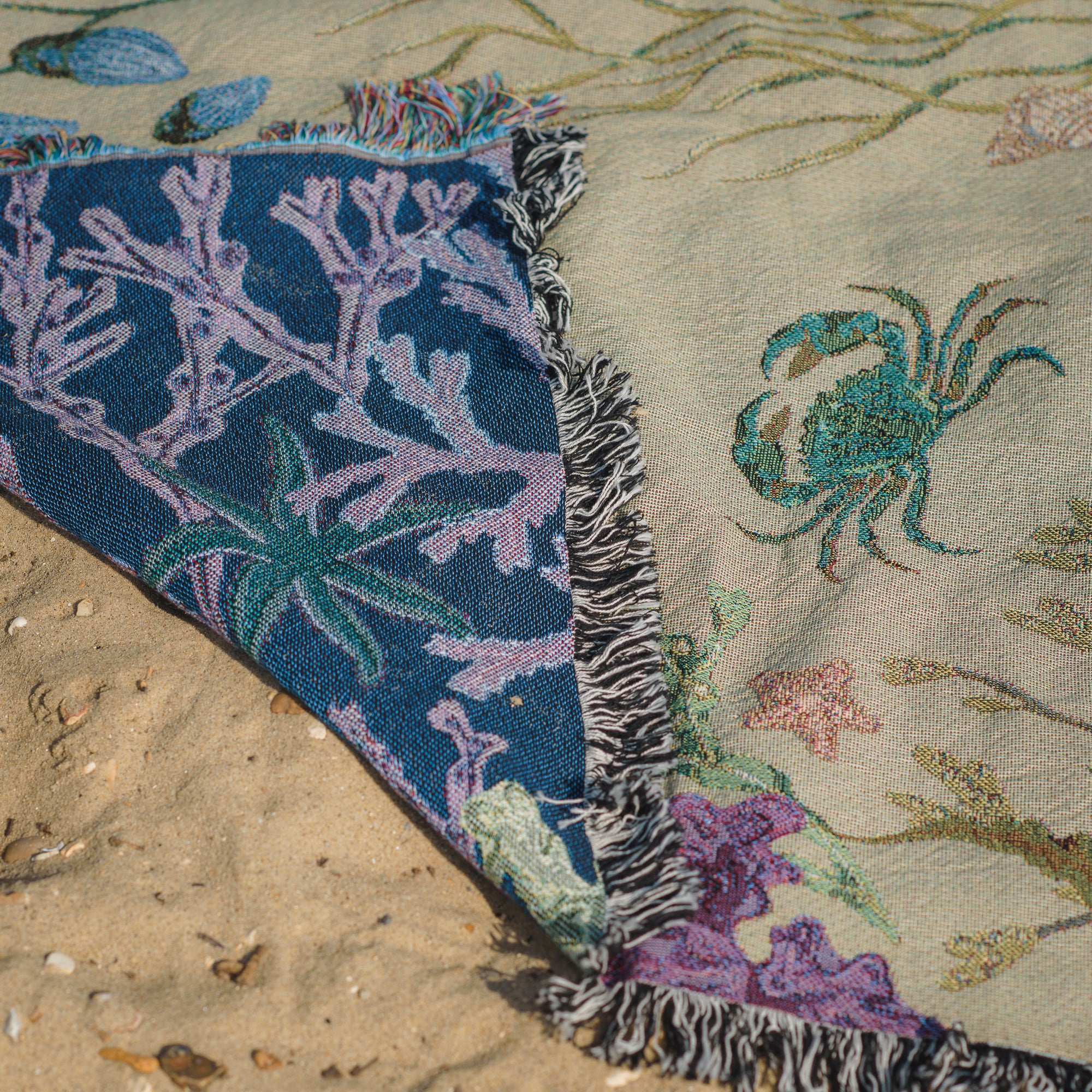An Arcana Intertidal Sand blanket laying on the sand showing woven detail of a shore crab