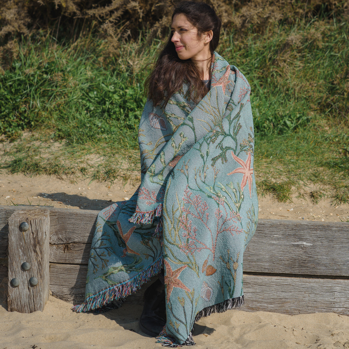 A woman sitting on a wooden bench with an Arcana Intertidal Star blanket.