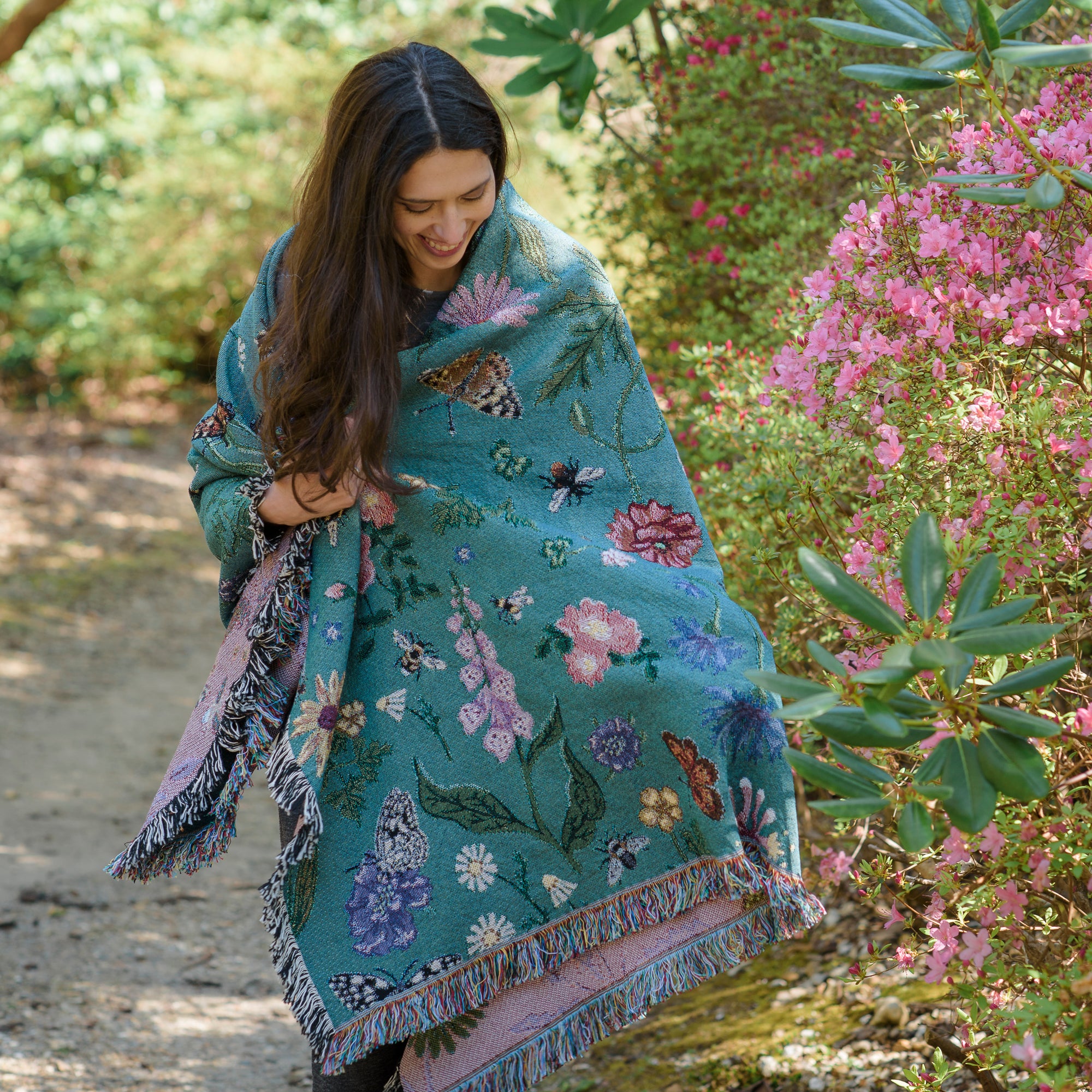 smiling woman wrapped in teal green woven blanket with butterflies and flowers mofif