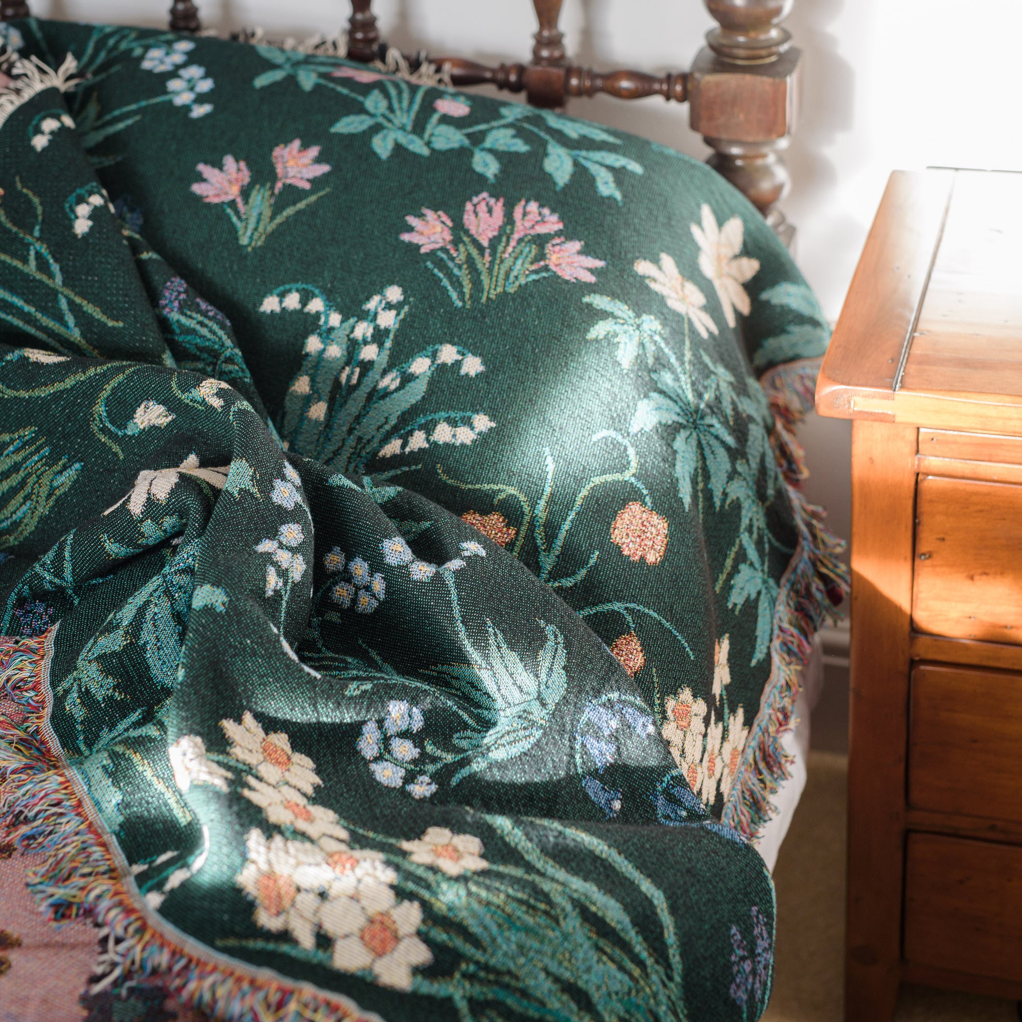 Spring flowers woven blanket in dark green with light coloured daffodils, forget me nots, lily of the valley, spread on anitique bed