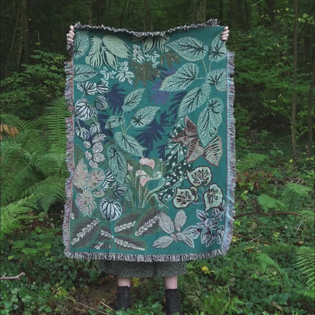 video of girl holding up woven wrap blanket with fringe featuring lots of different houseplants