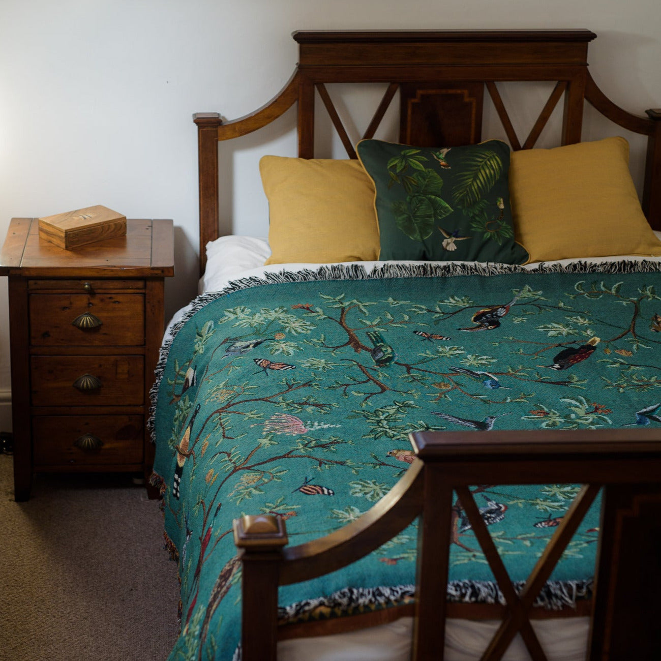 deep green tropical bird blanket across an antique wooden bed with gold cushions