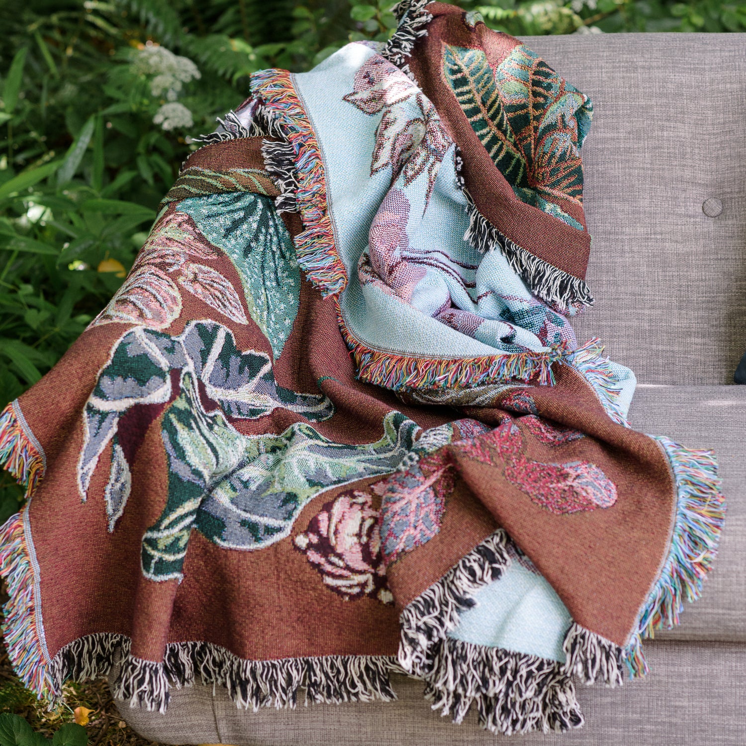 woven throw blanket in burgandy and light blue featuring houseplants on a sofa.