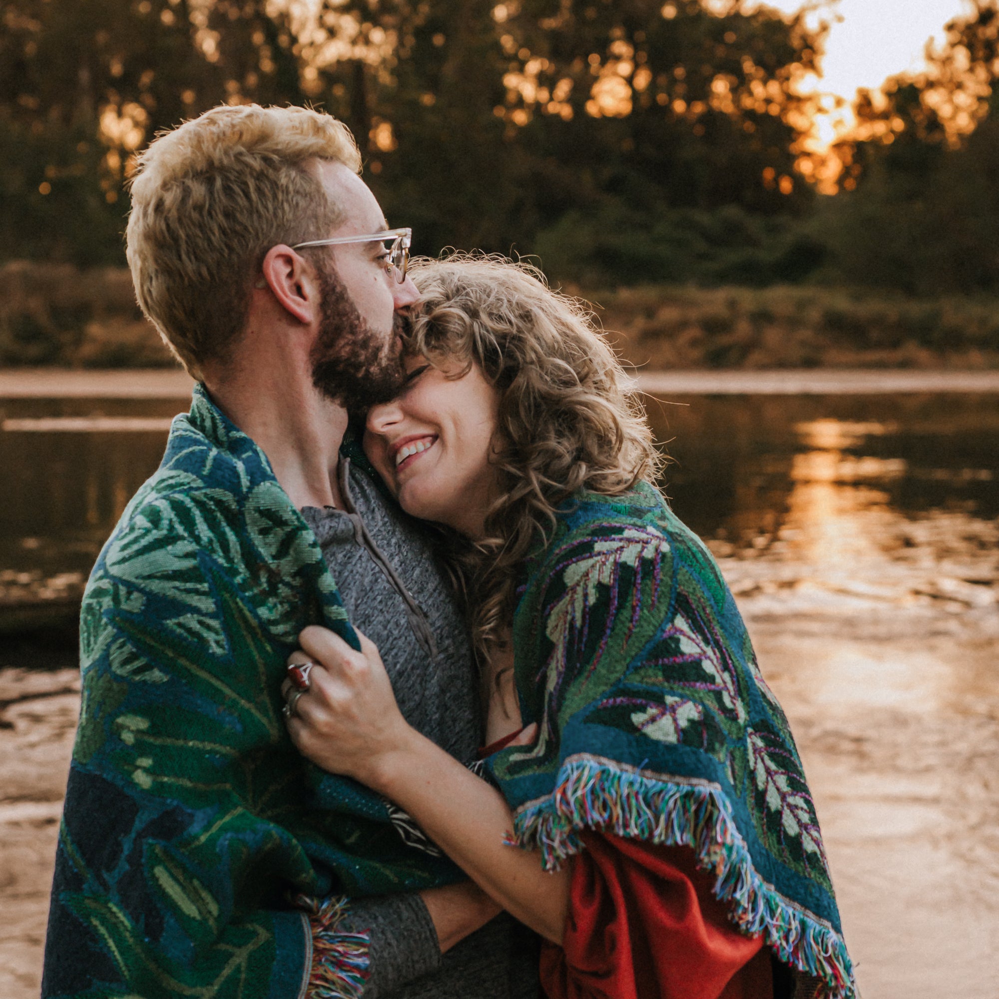 happy couple huging and laughing wrapped in teal and green woven blanket with leaves on