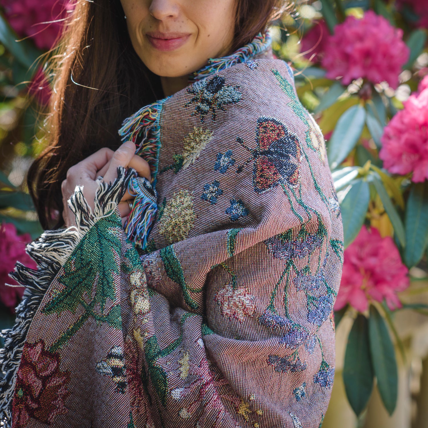 dusky pink woven wrap with bees, butterflies and flowers design wrapped around womans shoulders in summer garden