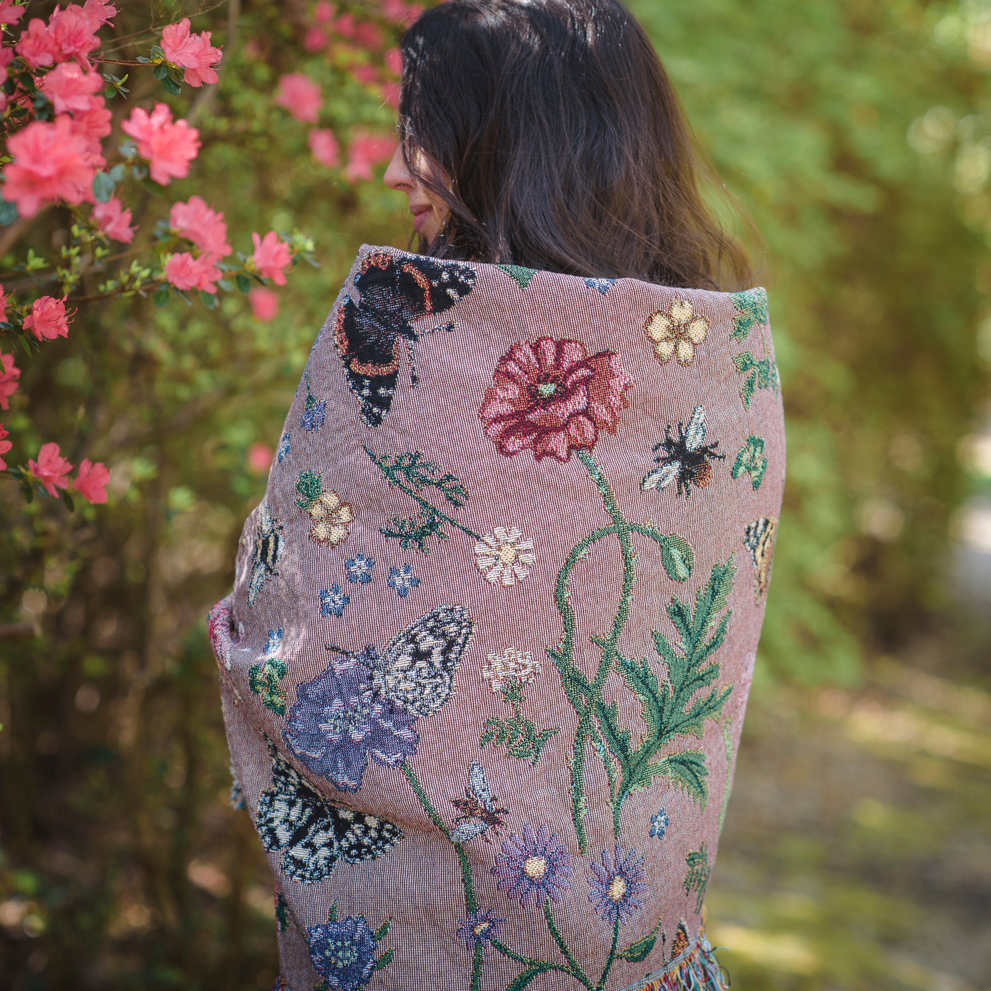 dusky pink woven wrap with bees, butterflies and flowers design wrapped around womans shoulders in summer garden