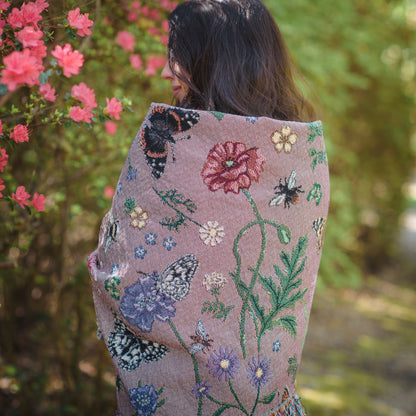 dusky pink woven wrap with bees, butterflies and flowers design wrapped around womans shoulders in summer garden