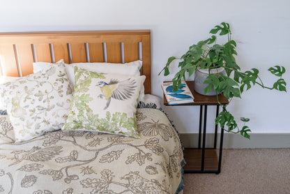 cream two tone woven blanket featuring oak woodland butterfies and birds spread across a bed in airy nature inspired bedroom