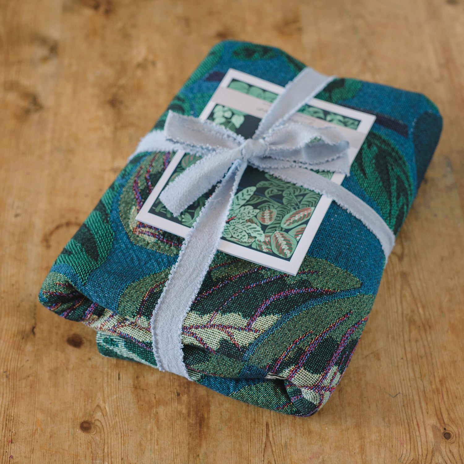 blue and green woven blanket featuring houseplants folded and tied with ribbon for the perfect gift