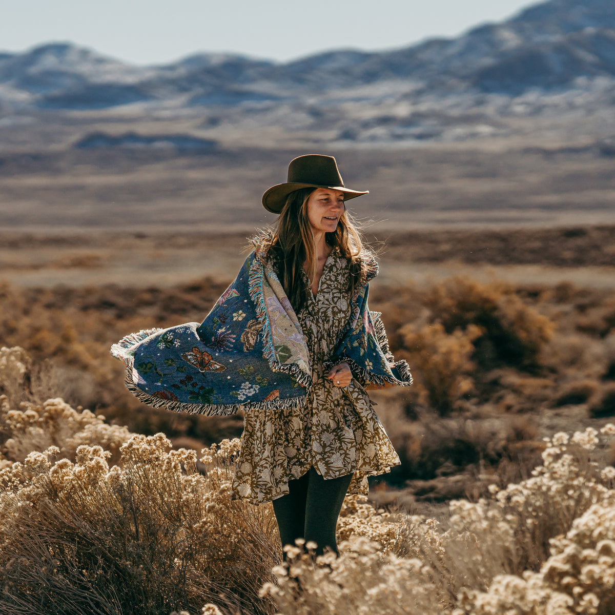 small dark blue woven wrap blanket with delicate moth and flower pattern around the shoulders of a woman in the mountains