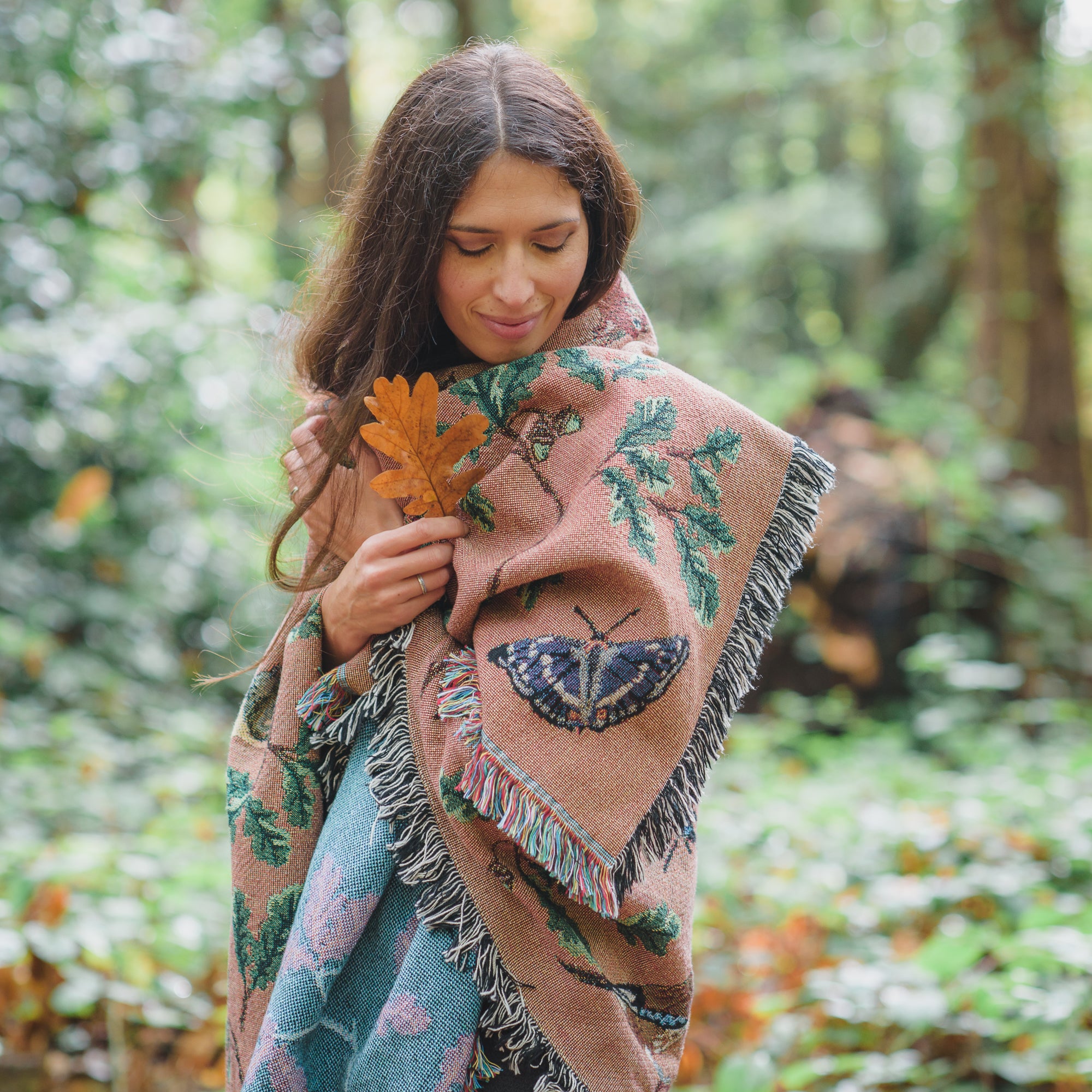 woman wrapped in russet coloured woven blanket with butterfly and oak standing in a woodland