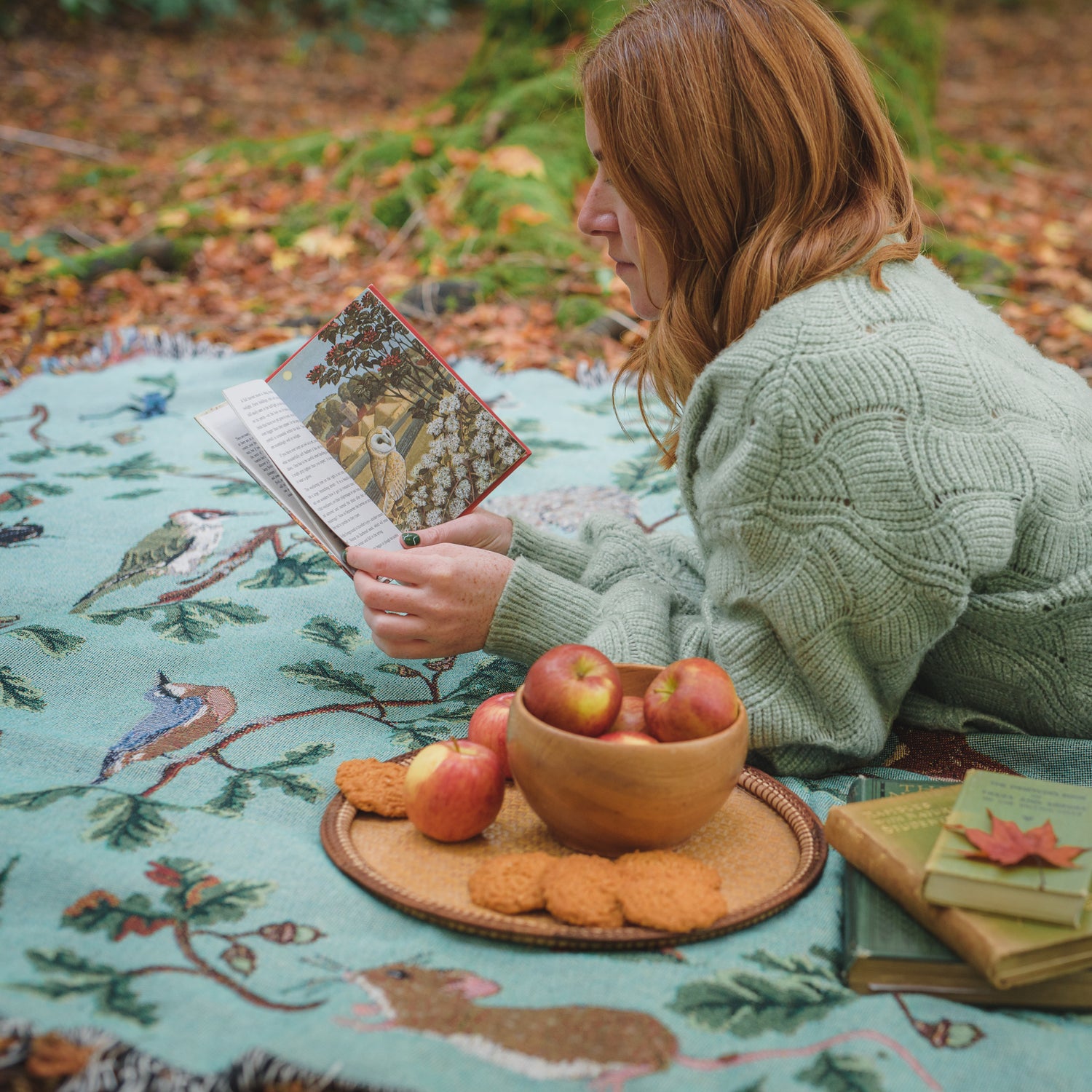 girl reading on Jade woven picnic blanket with red green woodpecker, oak, butterflies and nuthatch pattern